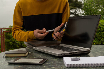 a young man pointing a pointer at his mobile and laptop at his outdoor work table