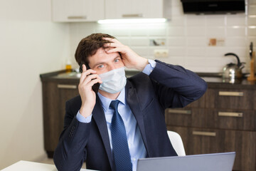 man in a mask holds his head with his hand and speaks on the phone, work at home