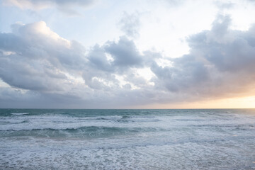 We are in Puglia, South Italy, Salento, view of the sea Jonio agitated, the waves foam approaching the coast in the golden hour, the sun colors the clouds orange.