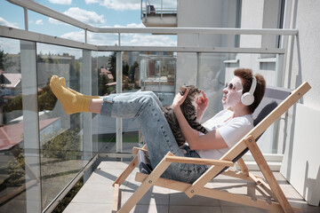 Home facial. Attractive girl with stylish hairstyle applying facial mask on face, playing wth cat and listening music on headphones.