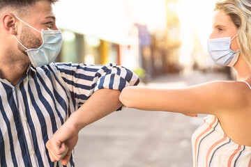 Young friends wearing face surgical mask doing new social distancing greet with elbow for...