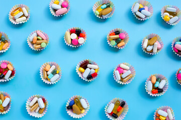 Colorful tablets with capsules and pills in cupcake wrappers on blue background.