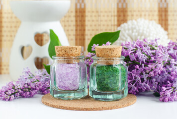 Obraz na płótnie Canvas Two small vintage glass bottles with purple and green bath salts (epsom salt, foot soak) and lilac flowers. Copy space.
