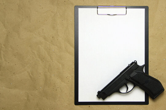 A tablet with a white sheet of A4 format with gun on a beige craft paper. Concept of the legal system, criminal organizations, security services. Stock photo with empty place for your text and design.