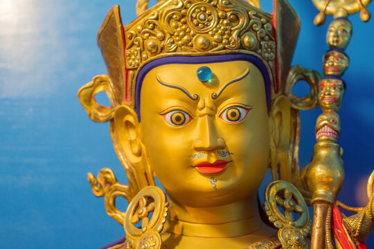 Gold statue of tibetan buddhist master Guru Rimpoche or Padmasambhava with blue background.