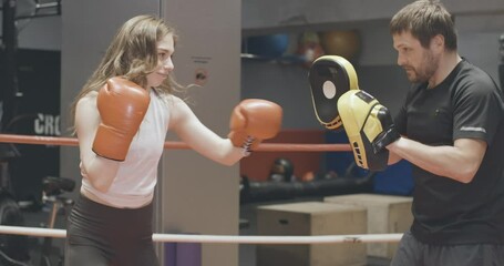 Sparring of cheerful female boxer with coach in training gloves on ring. Side view portrait of athletic strong Caucasian woman exercising boxing in gym with personal trainer. Cinema 4k ProRes HQ. - Powered by Adobe
