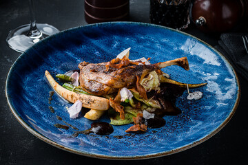 Fried duck leg with garnish on ceramic plate restaurant dark table