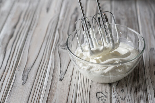 Woman whipping cream using electric hand mixer on the gray rustic wooden table