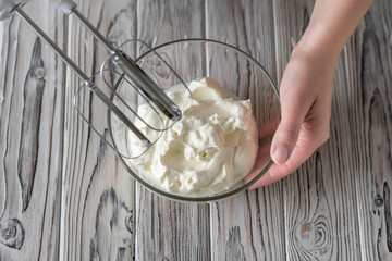 Woman whipping cream using electric hand mixer on the gray rustic wooden table. Flat lay