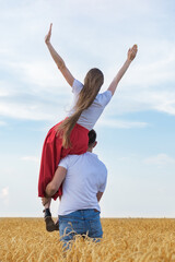 Young woman sits on shoulder of man and raised his hands up. Back view. Vertical frame