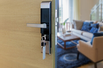 Digital door lock installed on wood door with key for security and access the room. Door wood texture with electronic door lock opened in front of blur living room. Selective focus.