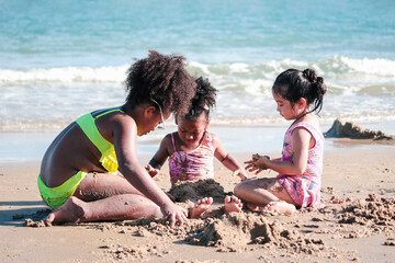 Cute kids having fun on sandy summer with blue sea, happy sister making sand castle, playing with sandat on tropical beach