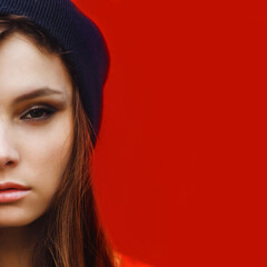 portrait of a beautiful girl in hat and striped sweater on a red wall outdoor