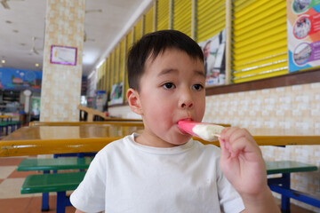 An Asian boy is wearing a white shirt eating ice cream.