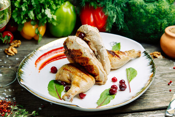 Restaurant dish with vegetable decor on a wooden background. Tobacco chicken with sauce and herbs on a plate.