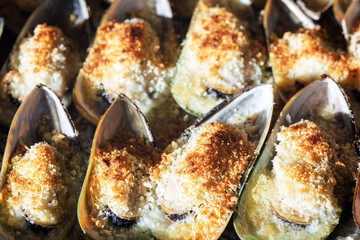 Mussels baked with parmesan, bread crumb and herb butter . Food background. Mediterranean cuisine. Concept for a tasty and healthy meal. Close up.