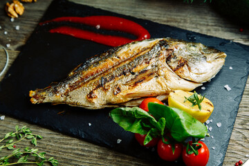 Restaurant dish with vegetable decor on a wooden background. Sea fish fried on a plate with sauce.