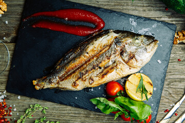 Restaurant dish with vegetable decor on a wooden background. Sea fish fried on a plate with sauce.