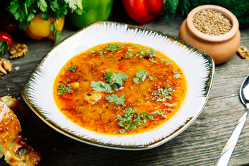 Azerbaijani restaurant dish with vegetable decor on a wooden background. Soup in a clay pot with herbs.