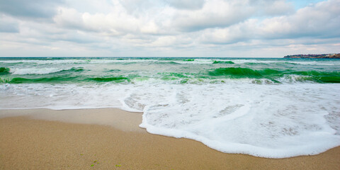 Fototapeta na wymiar sea tide on a cloudy evening. waves crashing sandy beach