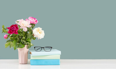 
Vase of flowers and a row of books with glasses for vision on a white wooden table