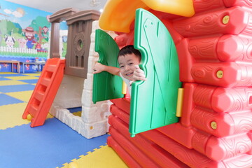 An Asian boy wearing a white shirt is playing a toy house in the playground.
