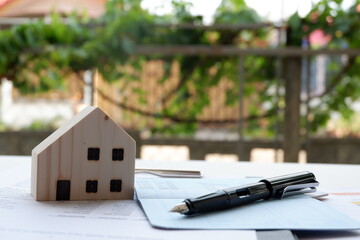 Model of house and pen placed on a bank book on table on blurred background