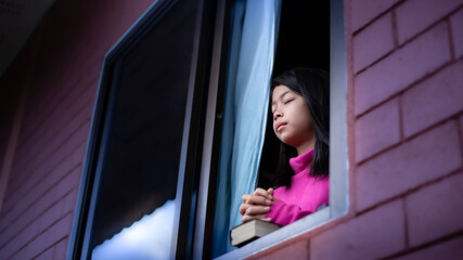 Asian young girl praying with the holy bible in the morning at window, Religion christian concept.