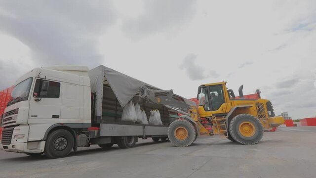A bulldozer unloads bags into a truck. Unloading goods from the truck. Bulldozer unloads goods from a car