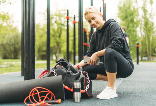 Attractive fit young blonde woman in black sport wear going to train on the street workout area
