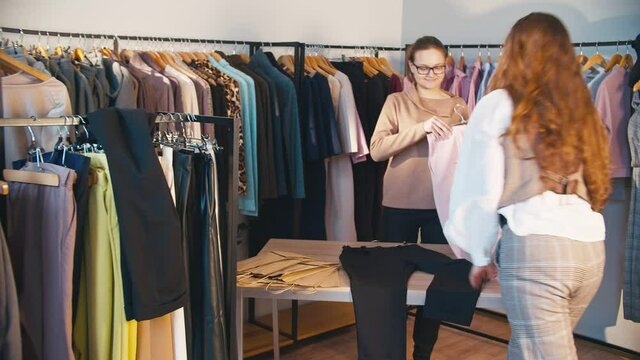 Woman shopping. Designer clothes. Cheerful female assistant packing trousers for buyer in showroom.