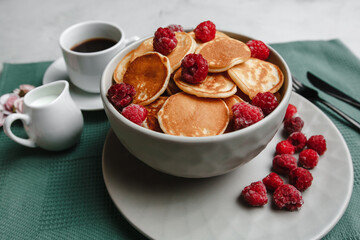 Trendy homemade Breakfast mini pancakes with raspberries and coffee on a white table. The view from the top. Side view. Space for text