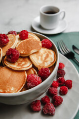 Trendy homemade Breakfast mini pancakes with raspberries and coffee on a white table. The view from the top. Side view. Space for text