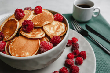 Trendy homemade Breakfast mini pancakes with raspberries and coffee on a white table. The view from the top. Side view. Space for text