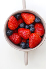 Ceramic bowl with fresh blueberries and strawberries. Top view, white background.