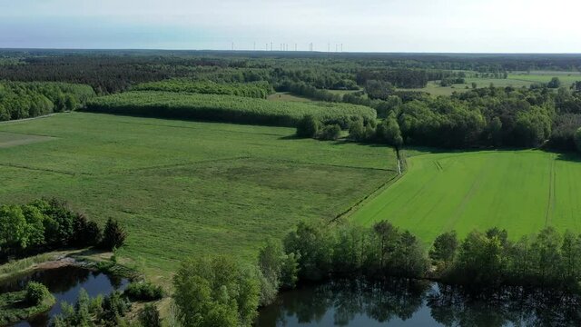 Aerial view of fields, meadows and forests in the flat landscape of Northern Germany, with ponds in the foreground and wind turbines on the horizon