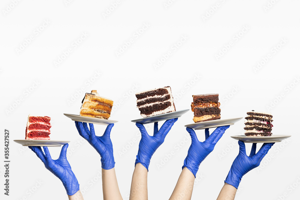 Wall mural Concept for cafe or bakery with desserts: plates with different cakes in gloved hands, Compliance with sanitary norms in restaurants, bakeries and cafes