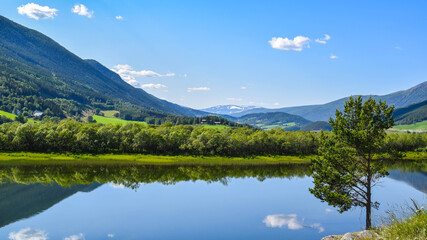 An idyllic, tranquil view of a peaceful Swedish valley in the beginning of summer. Blue skies, green, lush forests and a still lake that reflects the sky perfectly.