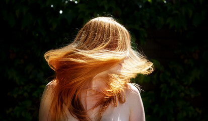 beautiful sexy redhead woman ginger, shaking her flying long hair against the sunny backlight