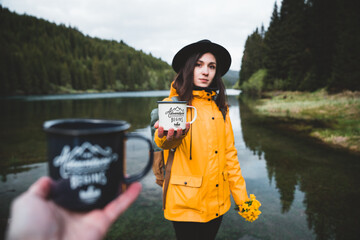 Beautiful girl with hat, backpack and yellow jacket holding outdoor mug or cup. Morning hot coffee...
