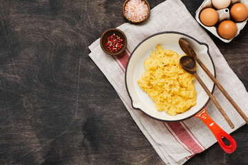 Scrambled eggs for breakfast on frying pan, dark wooden table background. Traditional English breakfast.Top view with cope space.