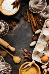 Baking and culinary background with flour, sugar, spices, nuts, cinnamon, wooden spoons and  rolling pin on an old dark wooden background. Top view with copy space.