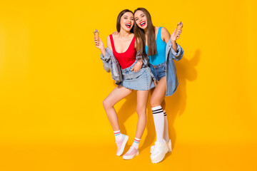 Full length body size view of her she nice-looking attractive glamorous cheerful cheery girls eating icecream having fun isolated on bright vivid shine vibrant yellow color background