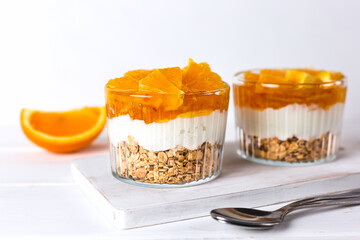 Breakfast of yogurt, jam, orange and granola on a white wooden table. Healthy food