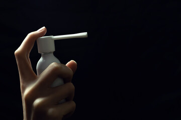 woman's hand holds a throat spray with a spout close-up on a black background with a copy of the space on the right