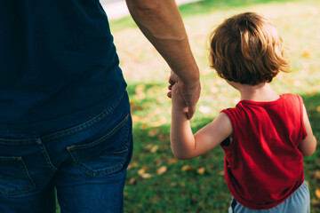 Father's day. Dad and son. Dad holds the hand of a little son in the park. Little child holding hands with his father outdoors. Family time. Close-up. Adult and child hands on natural background