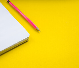 White notebook with pink pencil on a yellow background