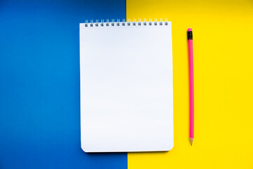 White notebook with pink pencil on a yellow-blue background