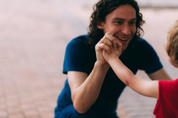 Father's Day. Blurred dad with his little son. Family walk with a child. Outdoor activities for family. Dad grabs his son's hand in the street. Hands of father and small child.