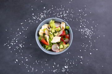 Fototapeta na wymiar Fattoush vegetarian salad in a gray bowl against black background. Top view. Levantine salad fattoush, which is prepared from dried pita with the addition of various vegetables and herbs. 